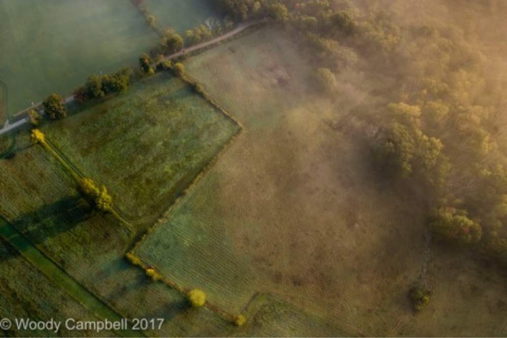 Drone image of farm field with light pink cloudy mist on the right