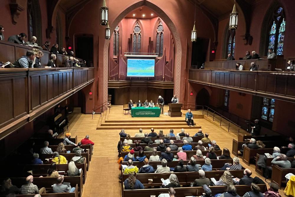 Audience sitting in a large chapel with a PowerPoint screen to the front and a group of panelists