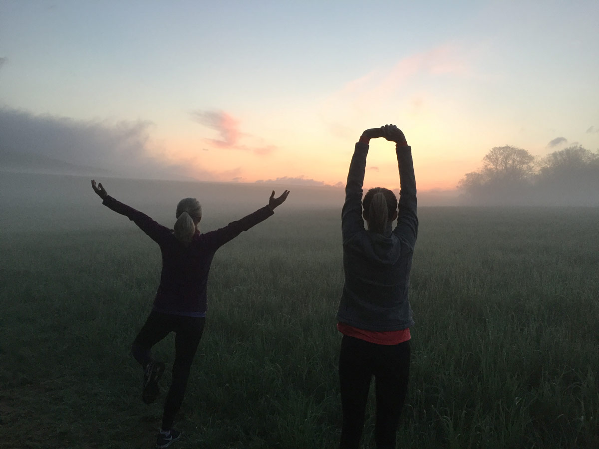 two women practicing yoga as the sun rises