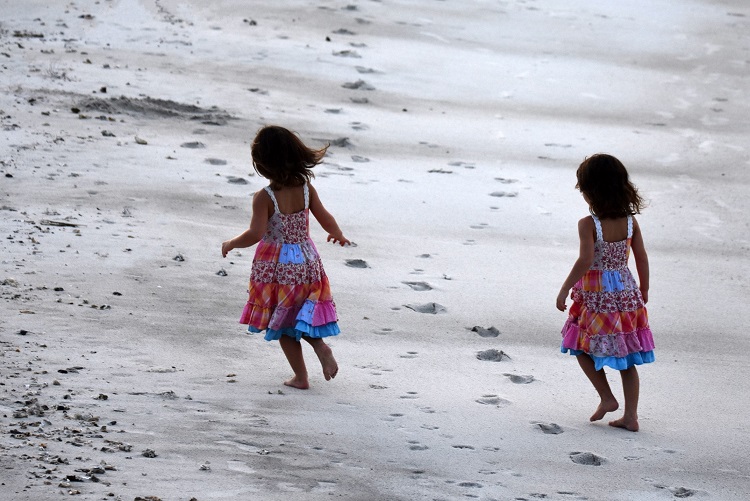 Two young girls in matching dresses making footprints in the sand