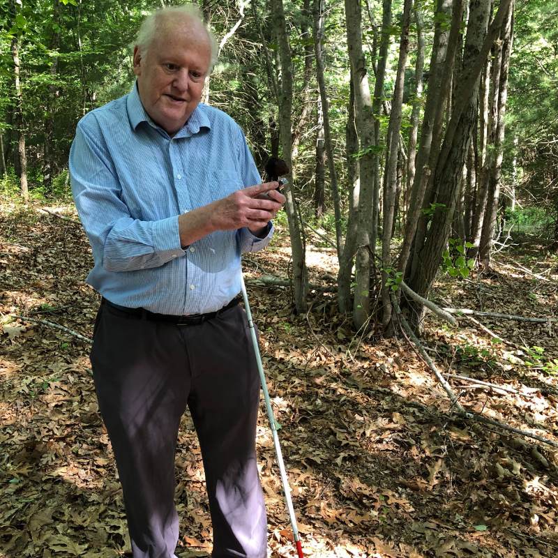 H Kevin Harkins holds a device to record bird sounds in the woods on a sunny day