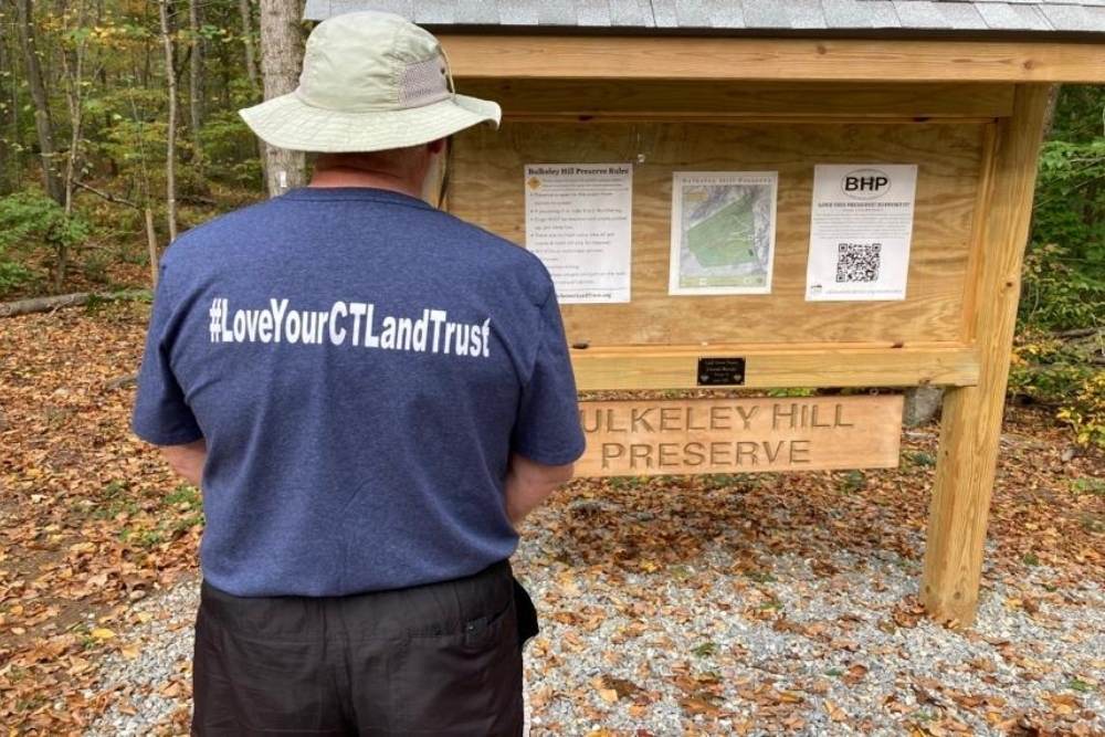 Man wearing a shirt that says #LoveYourCTLandTrust while looking at the trail kiosk at Bulkeley Preserve