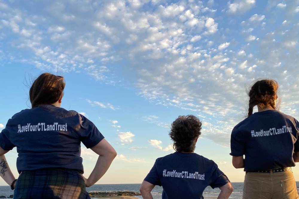 3 women standing at a beach at sunset wearing shirts that say #LoveYourCTLandTrust on the back