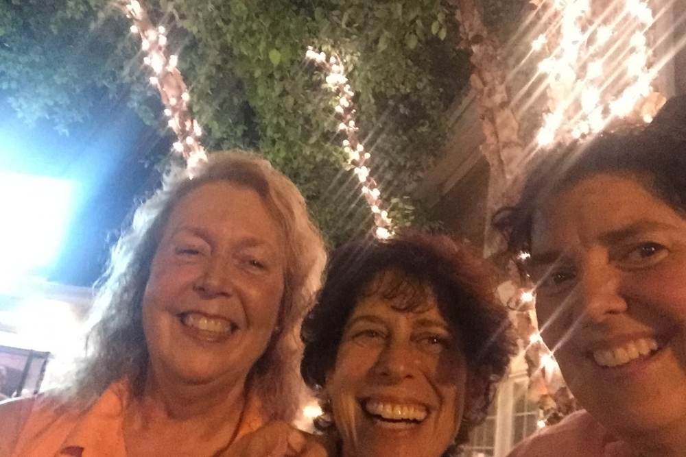 3 women smiling in front of a background of twinkle lights