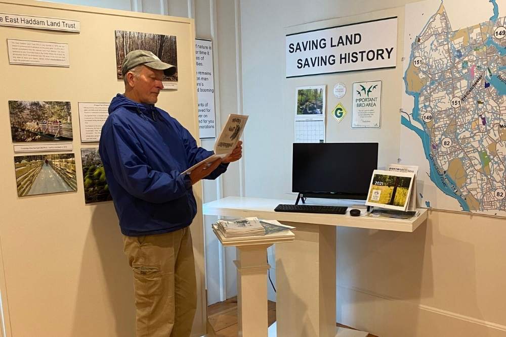 Man looking at a brochure at a Museum exhibit with a map and a sign that says, "Saving Land Saving History"
