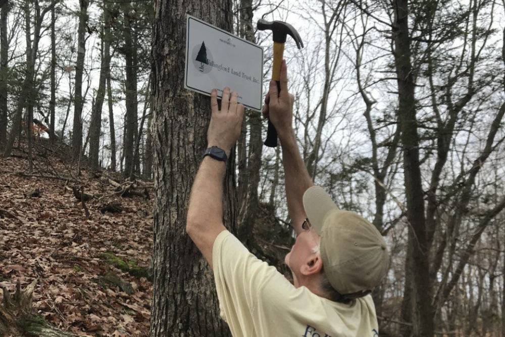 Man hanging a trail sign on a tree in the woods
